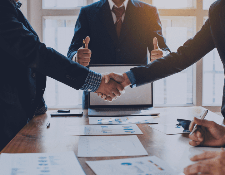 Three people shaking hands over a table with documents.